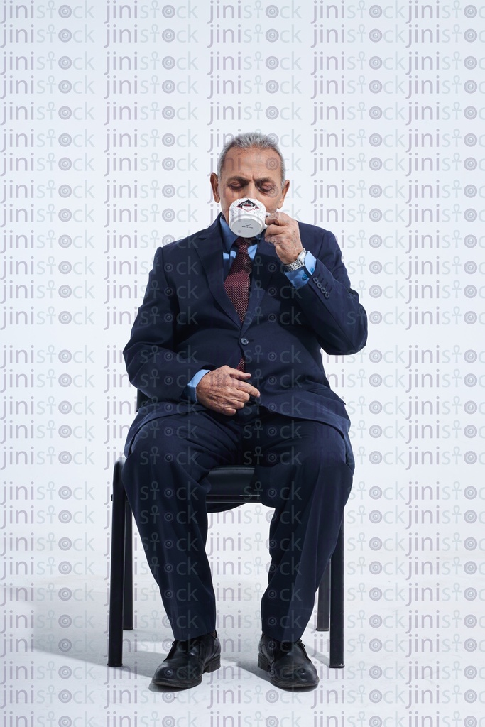 Old man in a suite drinking coffee sitting down