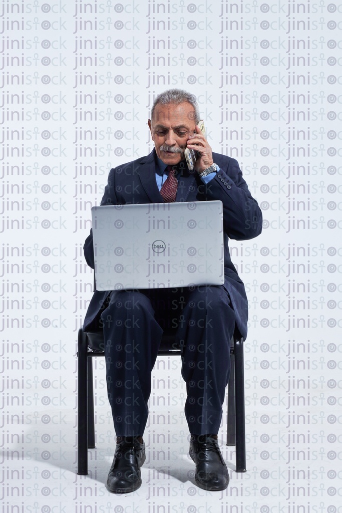 Old man in a suite manager talking on the phone while typing on laptop