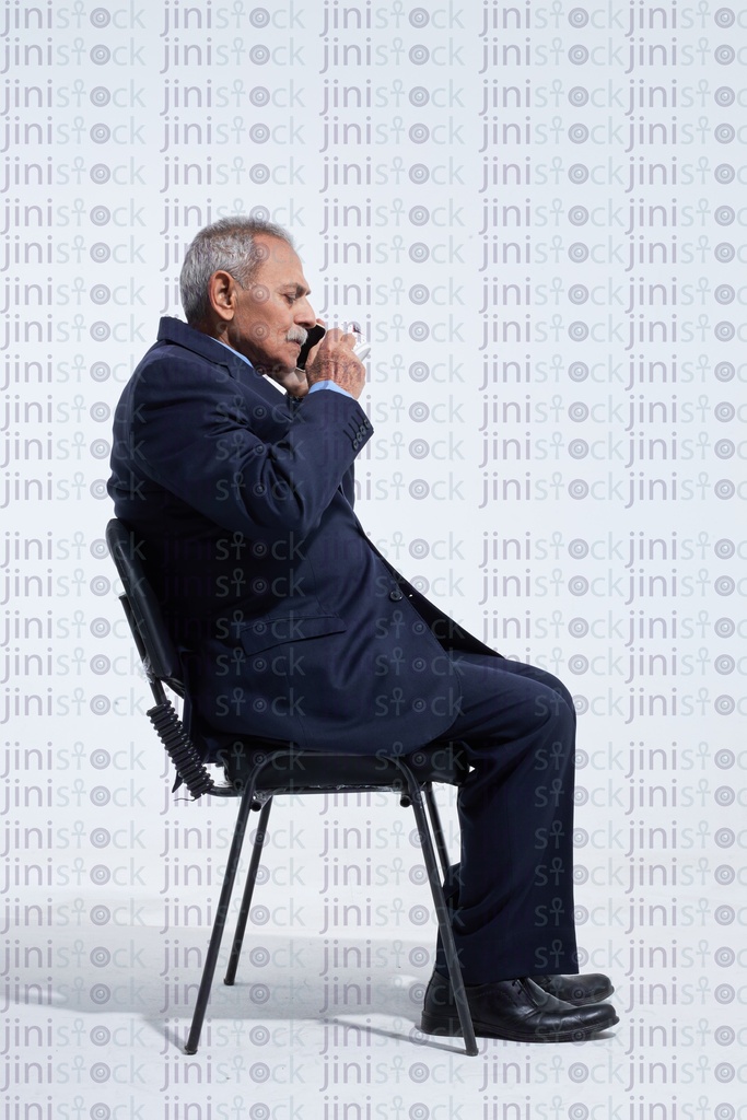 old man in a suite drinking coffee while talking on the phone