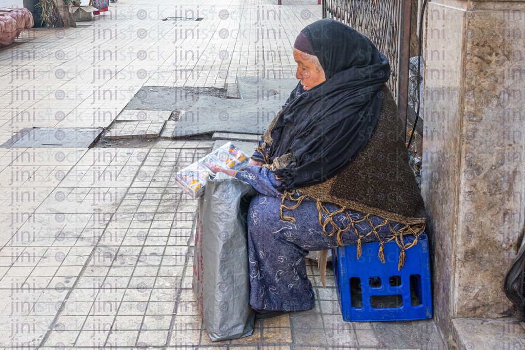 old poor woman sitting on the side of the street