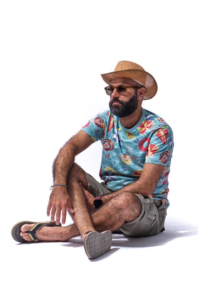 man sitting on the beach in eye glass and hat.