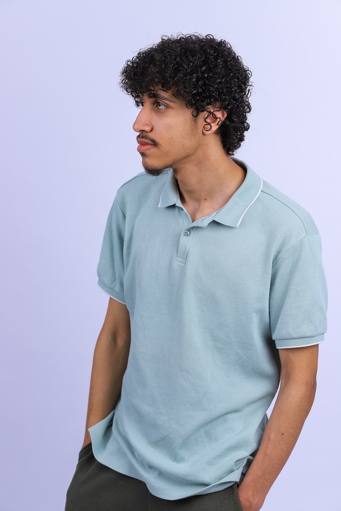 man with curly hair standing with hands in his pocket.