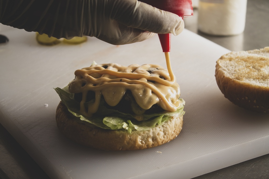 Close up on hands adding sauce to the burger