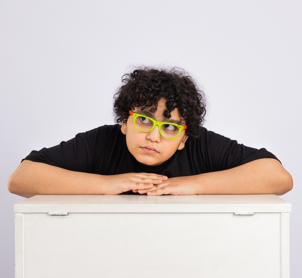 teen boy with glasses bored  leans on a desk