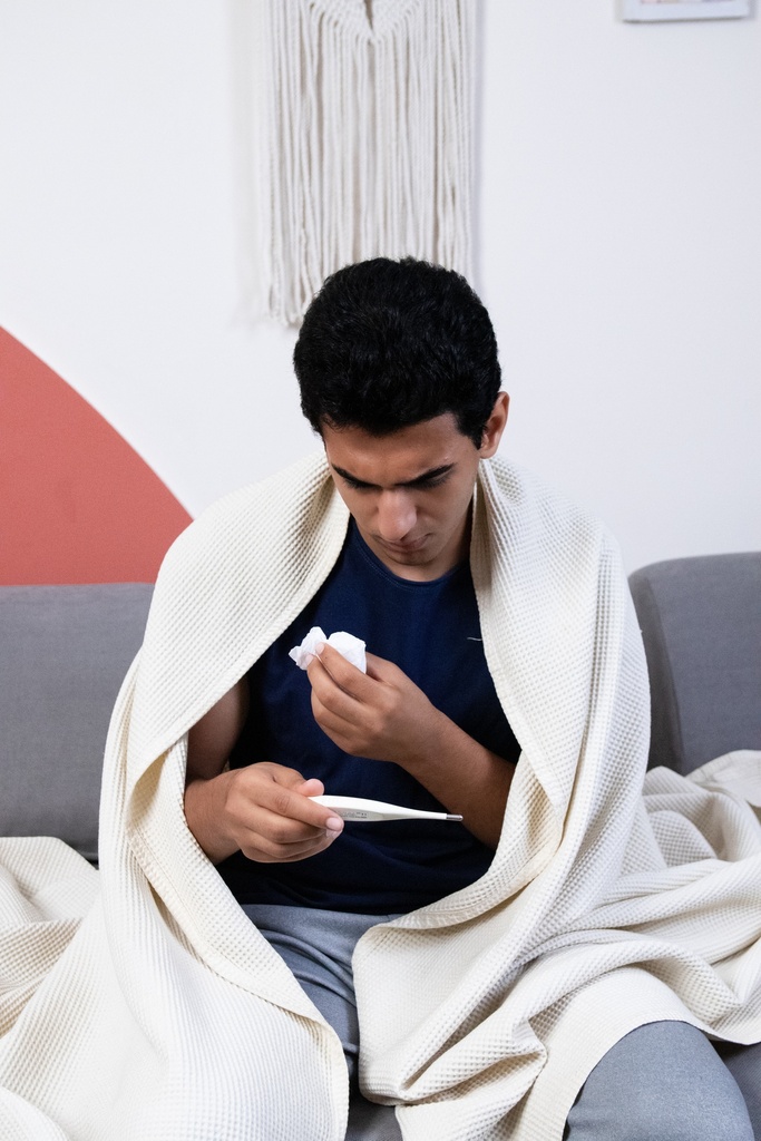 A sick young man checks the thermometer to measure his body temperature