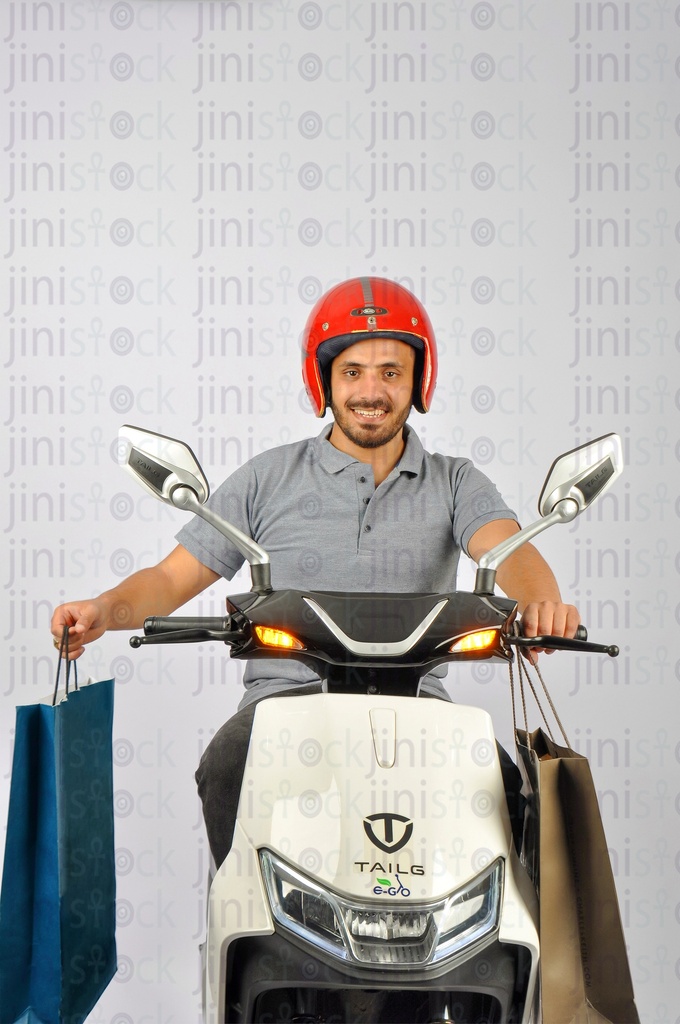 A male courier wearing red helmet riding white scooter and holding bags