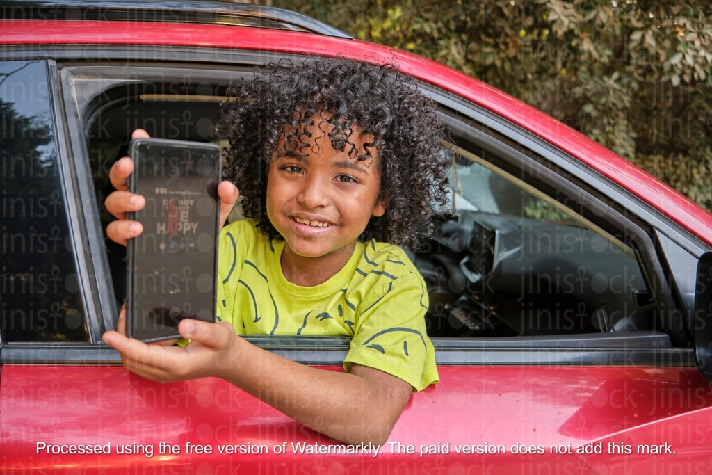 boy peaking from car window holding a mobile