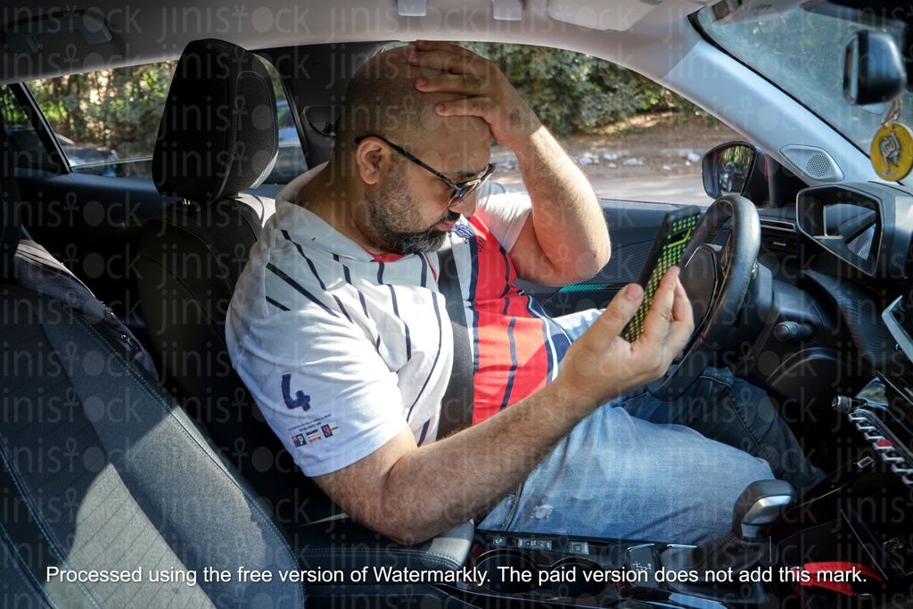 man looking in a car looking at his mobile sadly