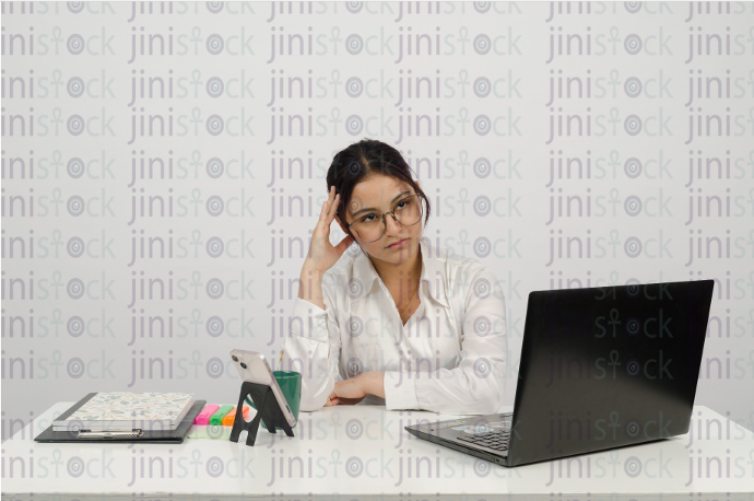 Woman sitting at a desk looking up with her hands on her head thinking - frontal close-up - stock image