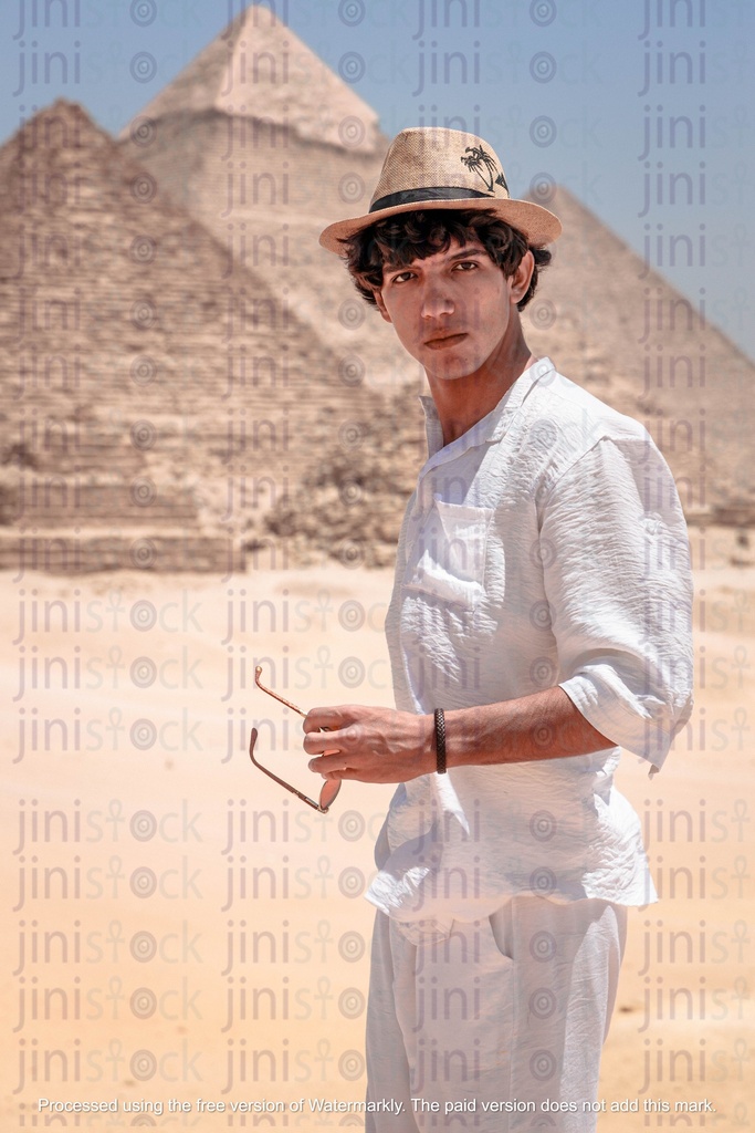 A man with a hat and holding sunglasses in his hands infront of the pyramids