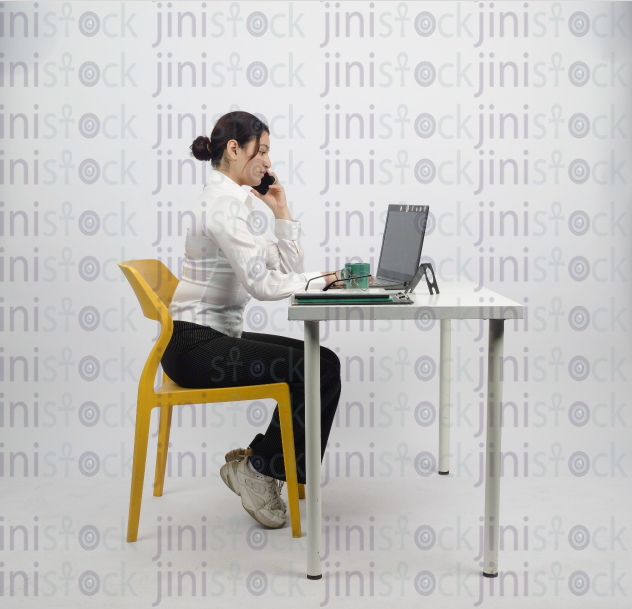 Woman sitting at desk - writing - laptop next to her - talking on mobile phone - close side shot -stock image