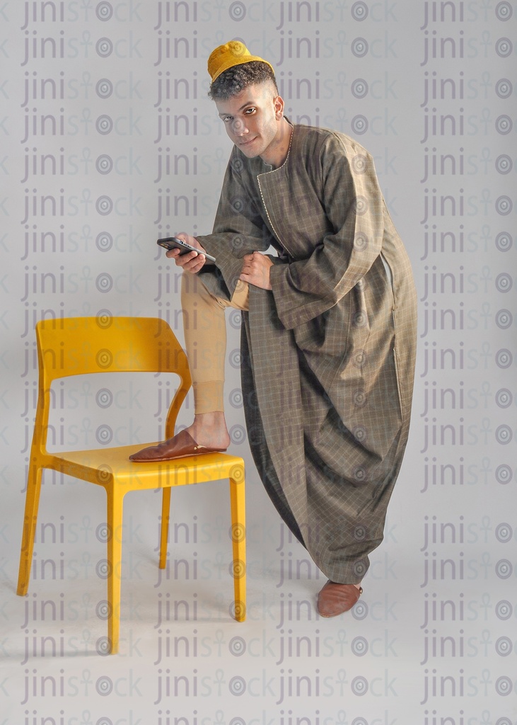 an Egyptian farmer putting his leg on a chair and holding a cell phone