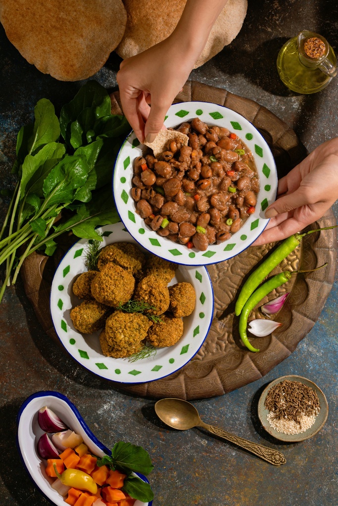 woman hand eating from the foul plate that is on an oriental egyptian breakfast tray next to falafel