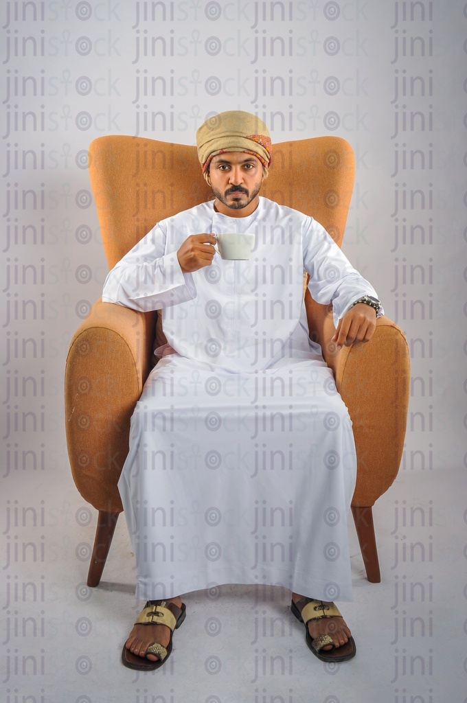 Omani man drinking a cup of coffee and sitting on a chair.