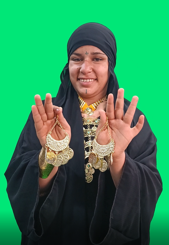 Video of a girl-Saidi girl holding an upper Egyptian accessories earring in her hand and looking in front of her and smiling.