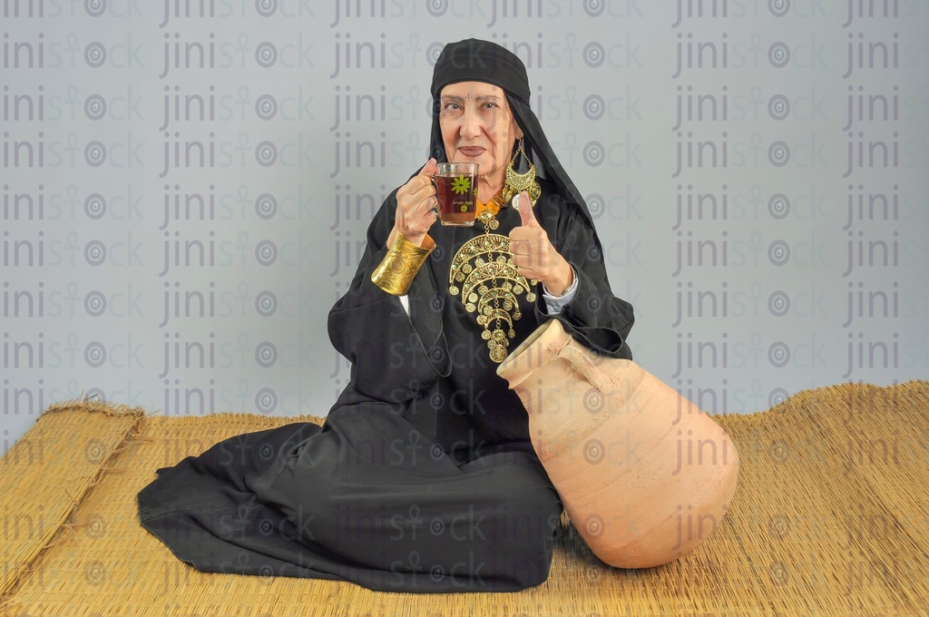 upper Egypt woman sitting on the rug holding tea and showing her thumb up