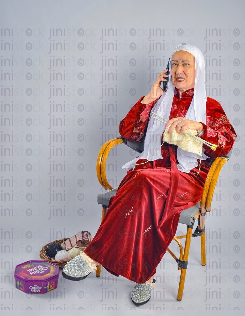 An Egyptian woman sitting on a chair and talking on a mobile phone with knitted sewing tools in her hand