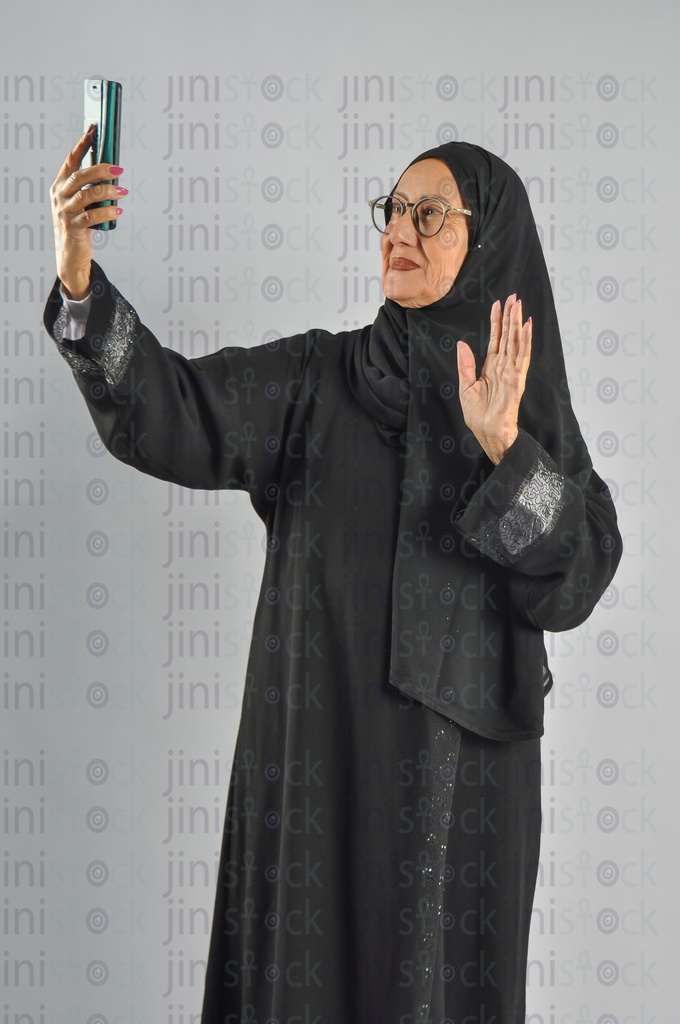 Saudi Arabian or Emirati woman or woman from the Gulf making a video call and waving or taking a selfie photo