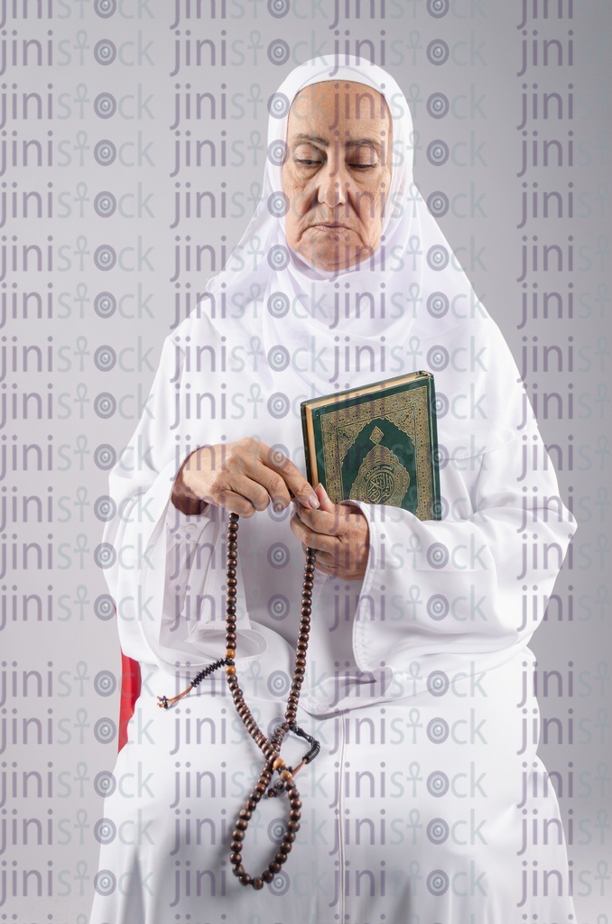 Old woman holding sabha and Qur'an while sitting on a chair 