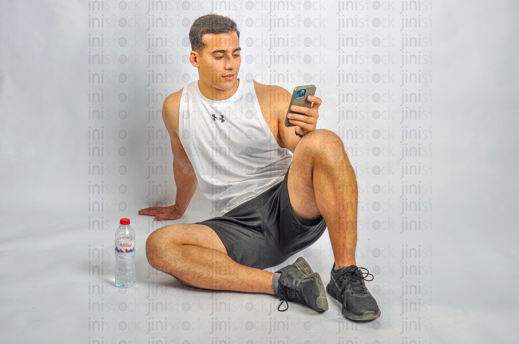 a Young athlete sitting on the land holding a mobile phone and texting