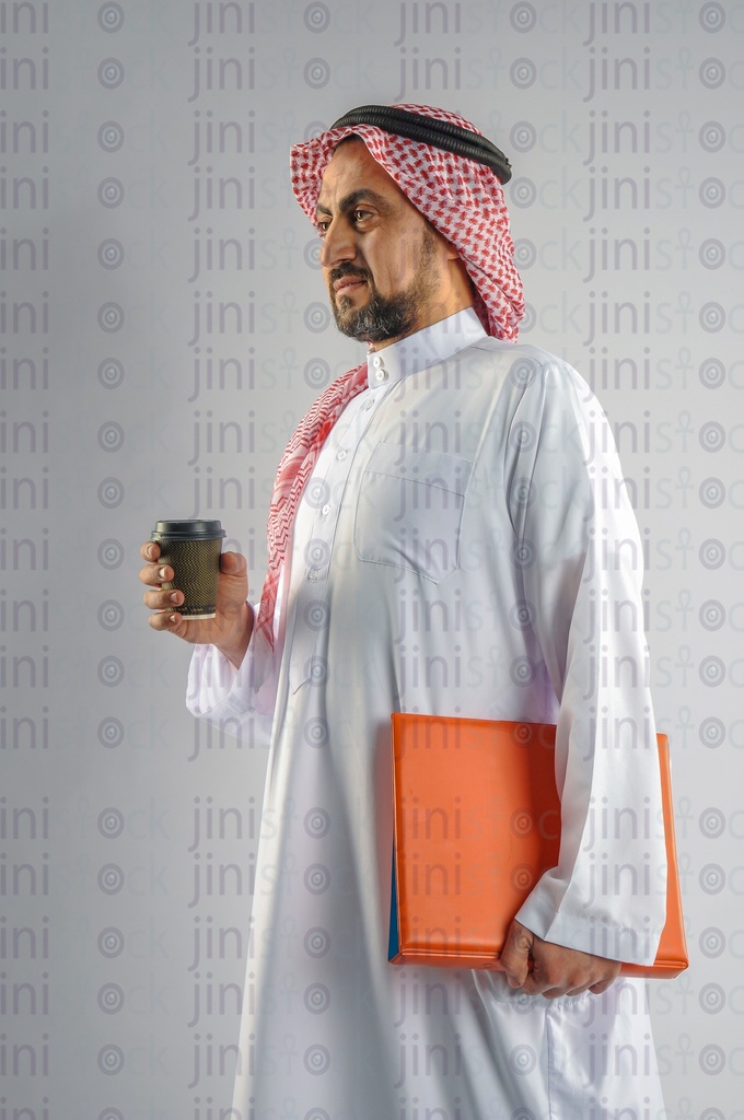 A man from gulf Saudi or Emirati holding a cup of coffee and a folder of work papers