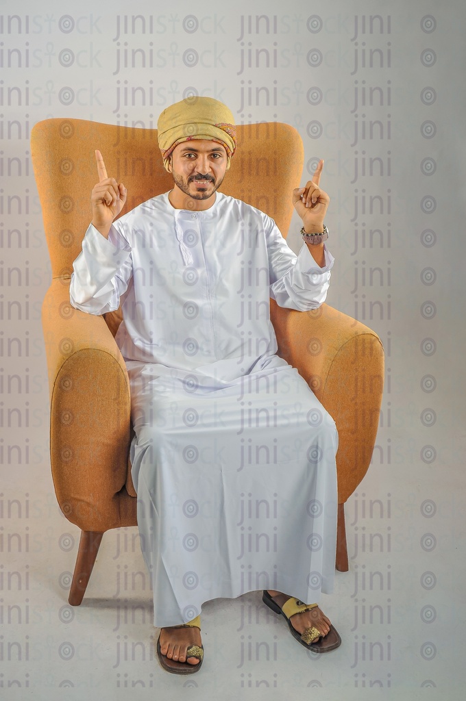 An Omani man wearing Omani clothes sitting on a chair and pointing at something top