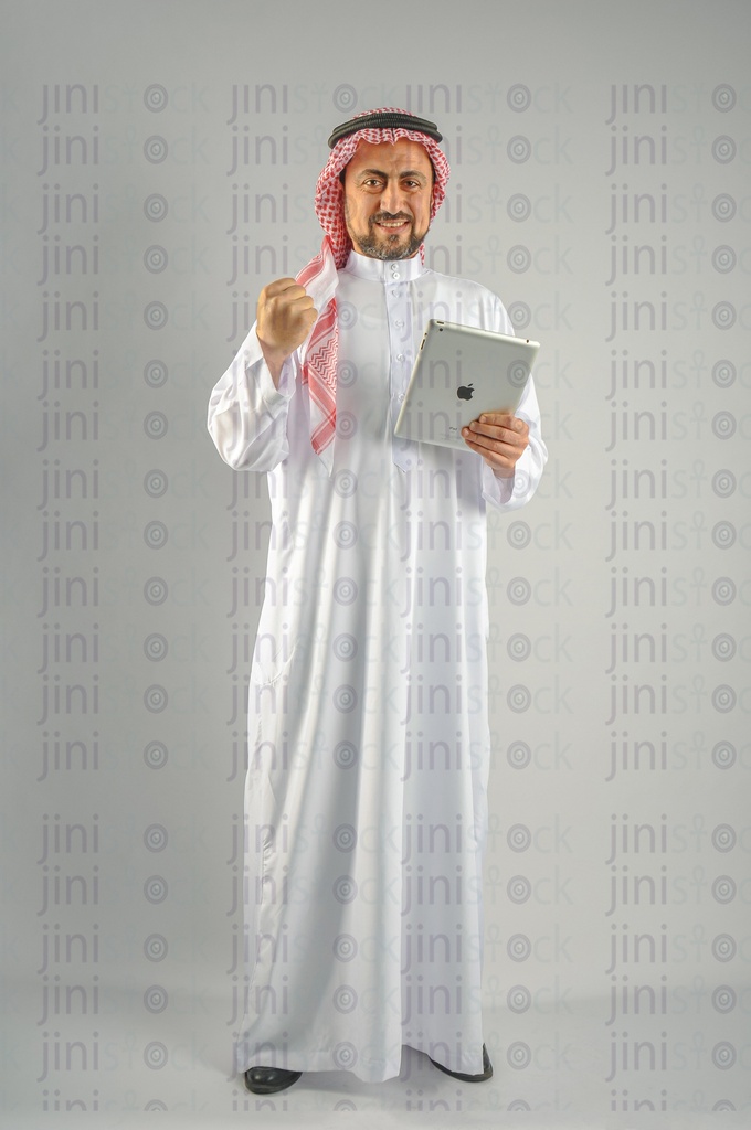 Khaliji Saudi Arabian or Emirati man or a man from the Gulf holding a tablet computer and looking at the camera and doing the winner sign