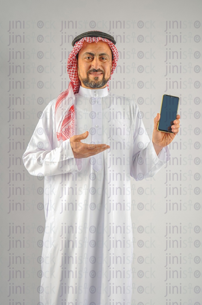 A man from the Gulf "Saudi or Emirati" holding a mobile phone to recommend a mobile application.