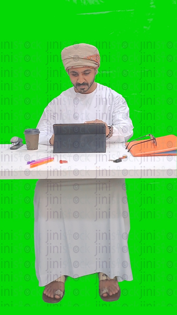 An Omani man from the Gulf sitting at a desk and working on a tablet at work in his office