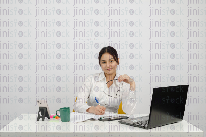 Woman sitting at desk - writing - thinking - holding glasses in hand looking forward - close-up frontal shot - stock image