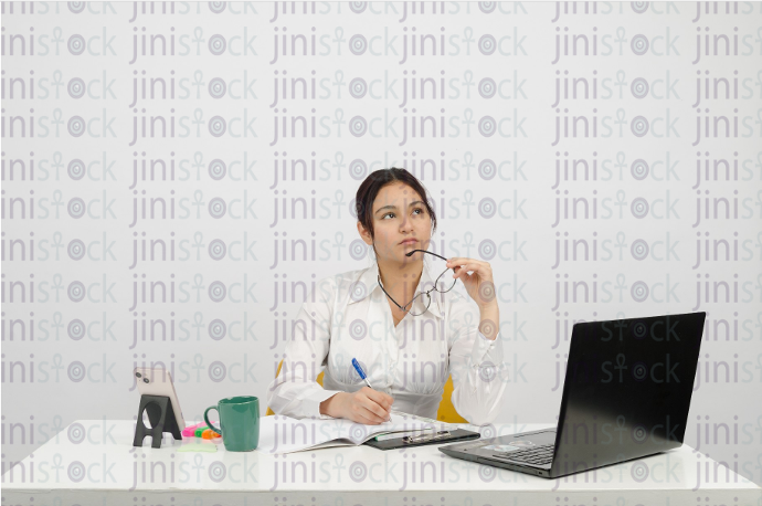 Woman sitting at desk - writing - thinking - glasses under her chin - frontal close-up - stock image