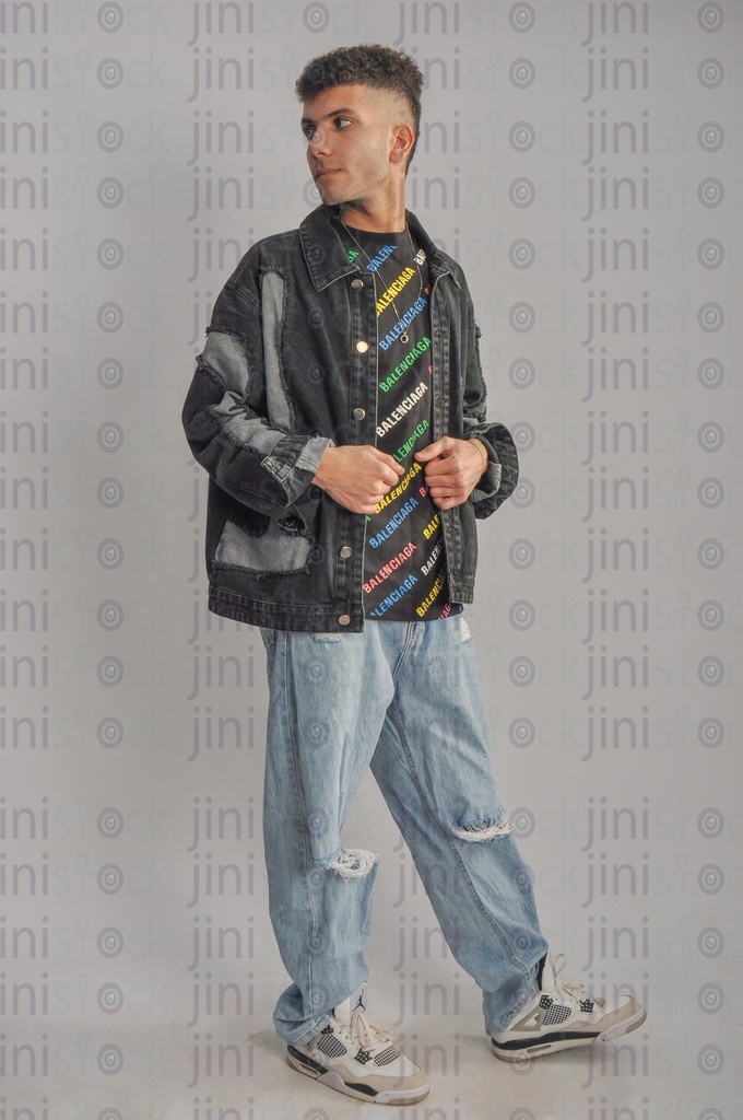 A cool Egyptian young man wearing trousers and a jeans jacket and holding his jacket