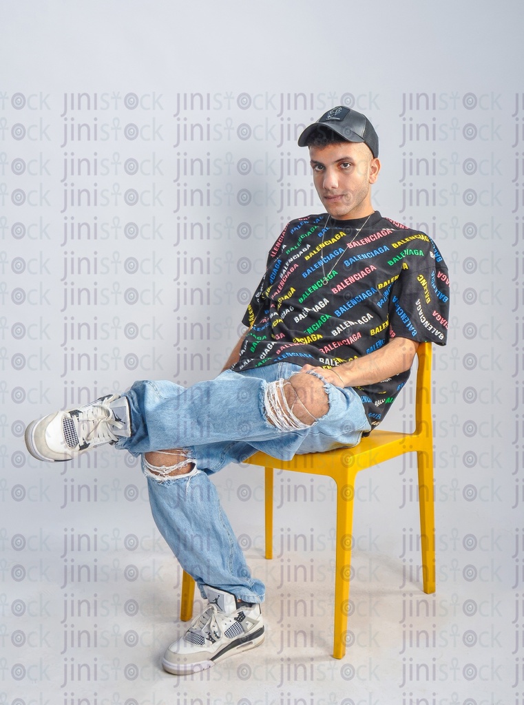 a cool young man wearing a cap, t-shirt, and jeans, and sitting on a chair