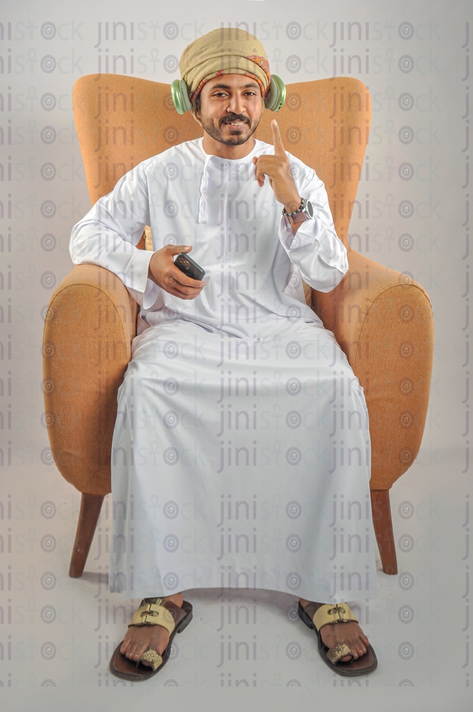 An Omani man from the Gulf wearing Omani uniform sitting on a chair and listening to songs.