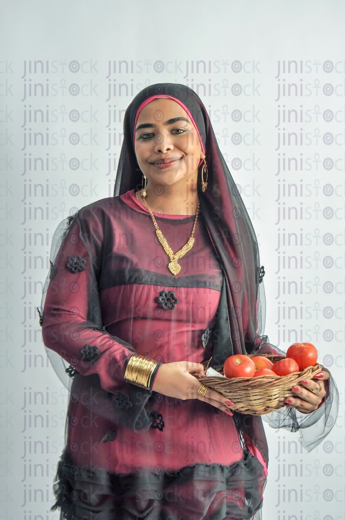 An Egyptian farmer girl or a Nubian woman from Egypt wearing Nubian clothes and holding a plate of tomatoes in her hands