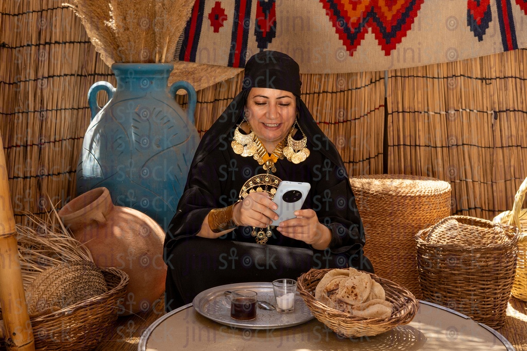 An Egyptian Bedouin woman in a wicker hut holding her phone