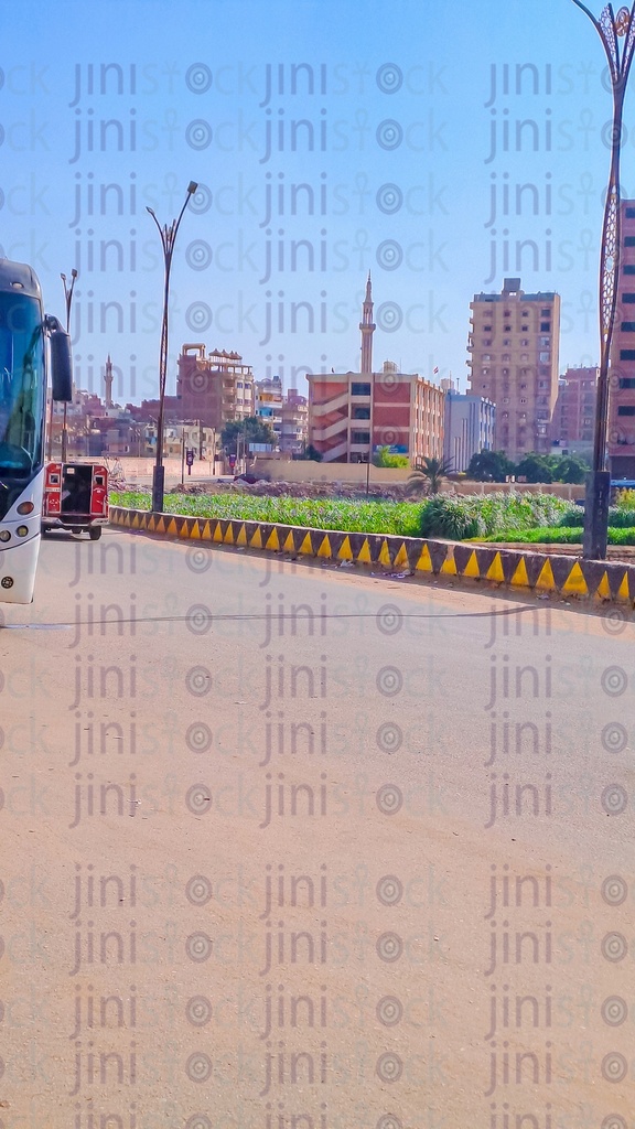 شارع بدون سيارات أو حافلات تمر به في الريف المصرى وفى خلفية الصورة مزرعة او حديقة ومبانى و مدرسه