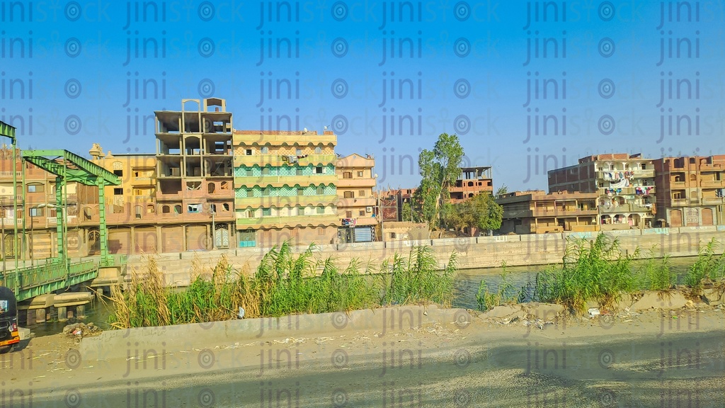A street in the Egyptian countryside with buildings, the Nile River, and plants