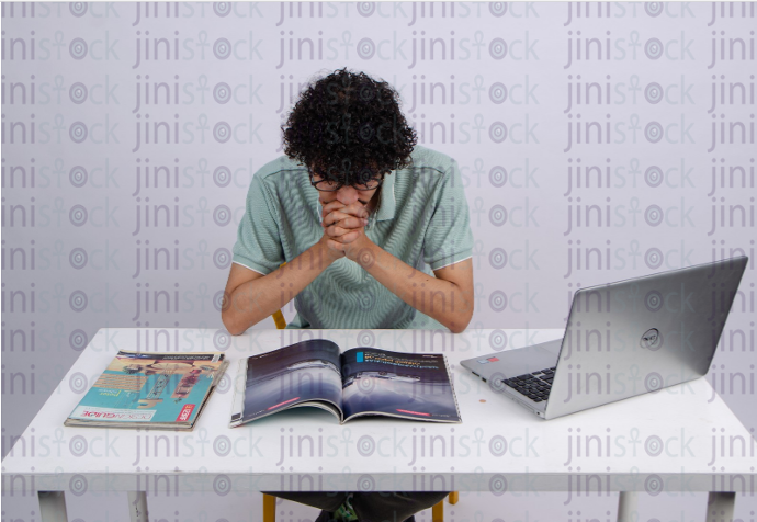 young man with curly hair reading on a desk - stock image