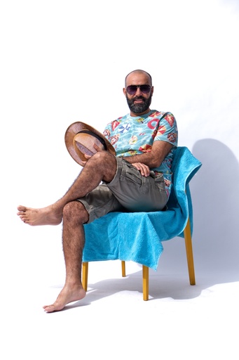 man sitting on a beach looking to the camera with his hat in his hand.