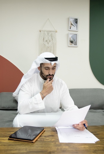 young khaliji man looking at a some papers and working on the couch.