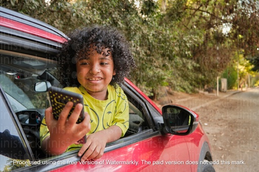 boy holding a mobile and peeking from the car window