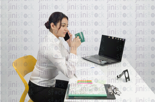 Woman sitting at desk, talking on mobile and thinking - close-up side shot - stock image