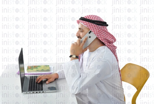 Khaliji man working on a laptop and talking on the phone in the office