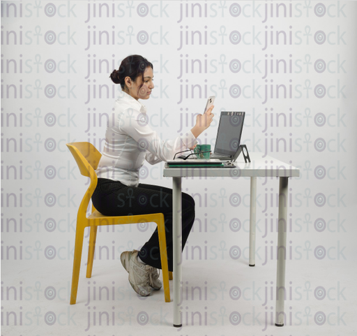 Woman sitting at desk with laptop in front of her and looking at mobile - close-up profile - stock image