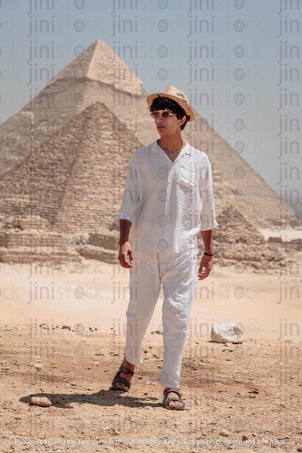 man in white posing in front of the pyramids