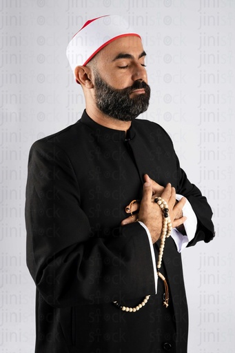 A sheikh holding a rosary with his hand on his chest closing his eyes