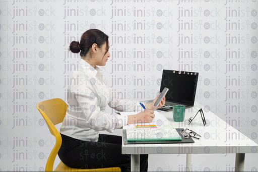 Woman sitting at desk, writing and looking at mobile - close-up side shot - stock image 