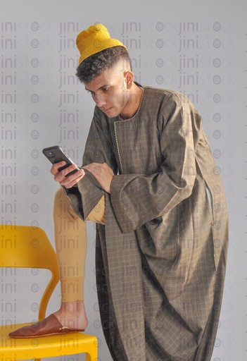 an Egyptian farmer putting his leg on a chair and holding a cell phone