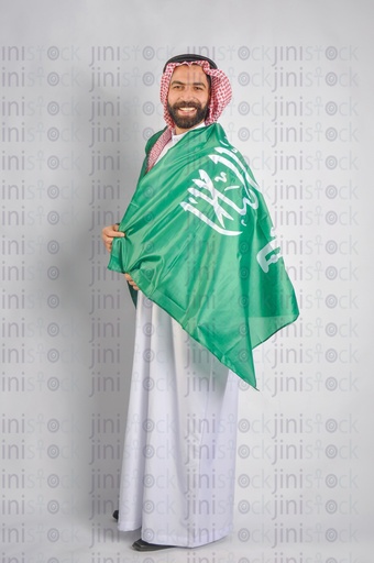 A Saudi man smiling and wearing the Saudi Arabian flag to celebrate the Saudi founding day.